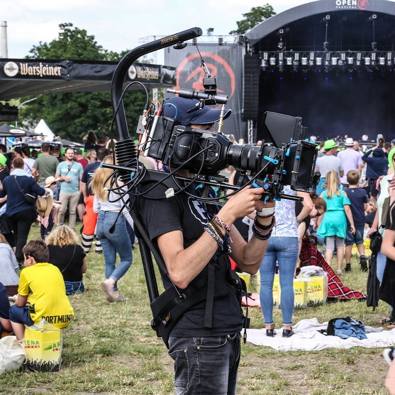  Kameramann Luzian Massarrat auf dem Uelzen Open R Festival, Menschenmenge und Bühne im Hintergrund.