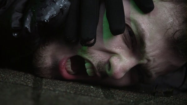 Das Gesicht eines laut brüllenden Mannes wird von einer behandschuhten Hand auf den Boden gedrückt.
