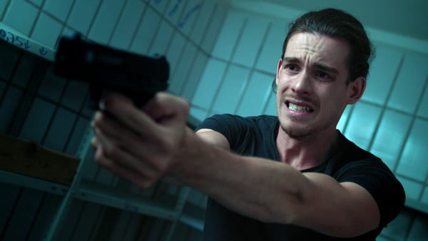 Ein junger Mann in einem finsteren Raum zielt panisch mit einer Pistole.