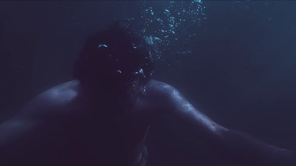 Eine Person treibt in der Dunkelheit unter Wasser. Blasen steigen auf.