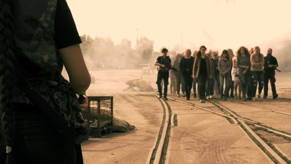 Eine Gruppe Gefangener wird von Bewaffneten über eine Gleisanlage getrieben.